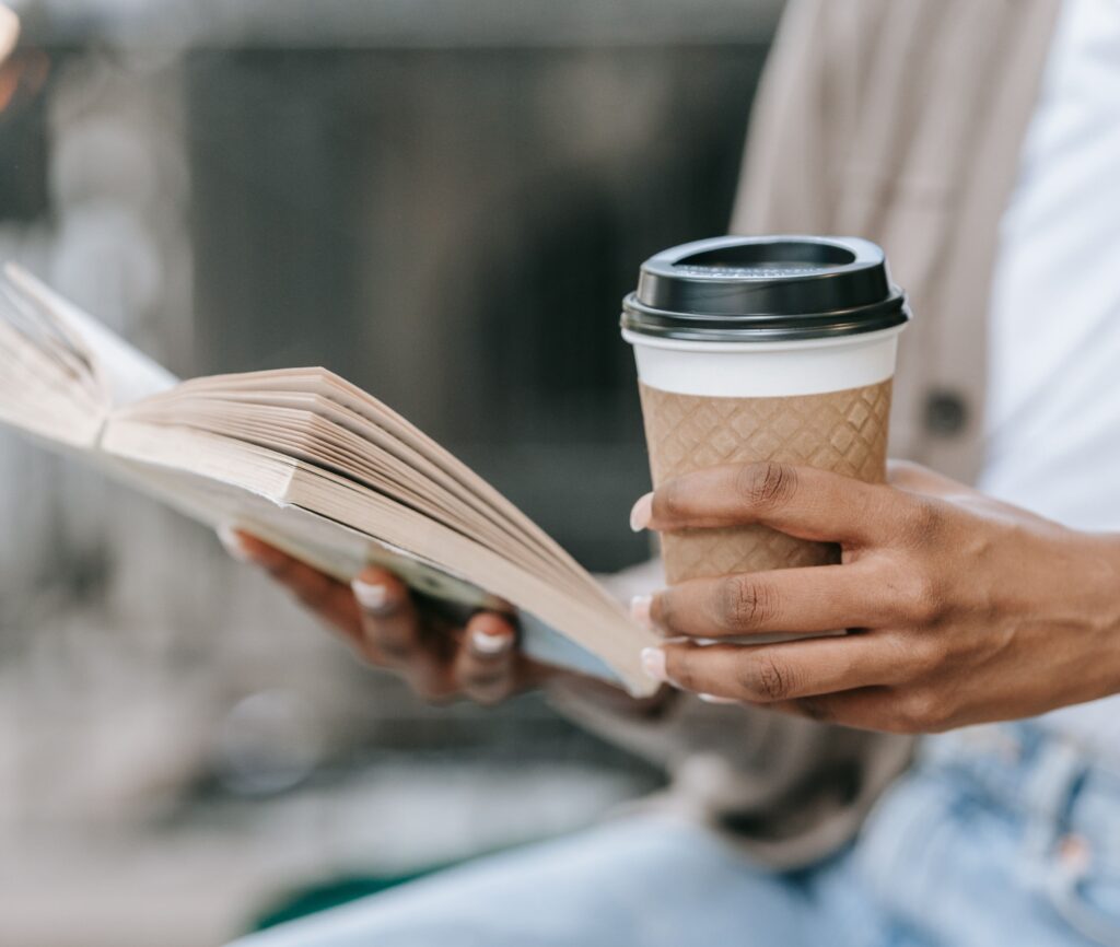 Uma mulher sentada lendo contos eróticos um livro e segurando um copo com outra mão.